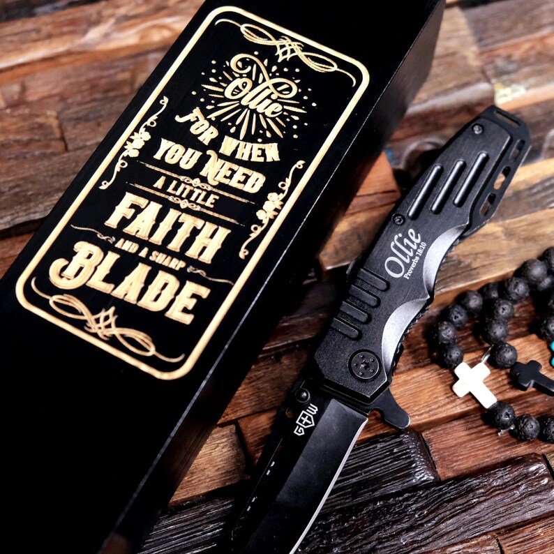 May include: A black wooden box with a gold inscription that reads "For when you need a little faith and a sharp blade." The box contains a black pocket knife with a silver blade and the name "Ollie" engraved on it.