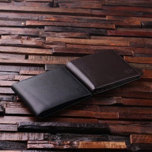 May include: Two black leather wallets on a wooden surface. One wallet is closed and the other is open, revealing a black interior.