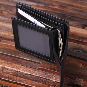 May include: A black leather wallet with multiple card slots and a clear ID window. The wallet is open and shows the interior compartments.