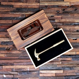 May include: A wooden box containing a gold-coloured hammer. The box features a plaque inscribed with the name "Ollie" and a quote about strength and resilience.