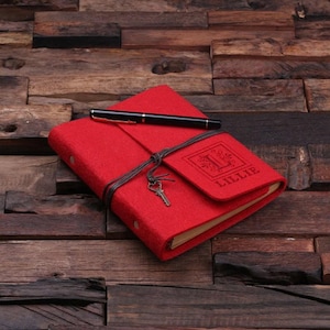 May include: Red felt journal with a brown leather strap and a key charm. The journal has a personalized inscription that reads "Lillie".