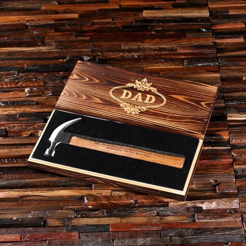 Pu&ograve; includere: Una scatola di legno con un martello all'interno. La scatola &egrave; incisa con la parola "DAD" e un design decorativo. Il martello ha un manico in legno e una testa in metallo. La scatola &egrave; rivestita in velluto nero.