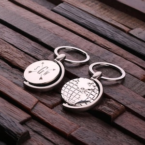 May include: Two silver spinning globe keychains. One keychain features a globe with a grid pattern and the other keychain features a circular disc with the initials "S.G.W." and three arrows pointing outward.