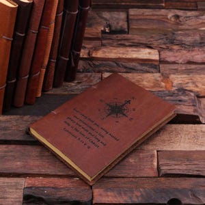May include: A brown leather journal with a compass design and a quote from Ephesians 5:17-18. The journal is closed and lying on a wooden surface.