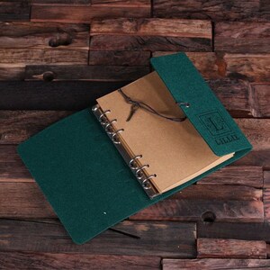May include: A dark green felt-covered notebook with a brown paper insert and a metal ring binding. The notebook has a leather strap closure and a personalized inscription that reads "Lillie".