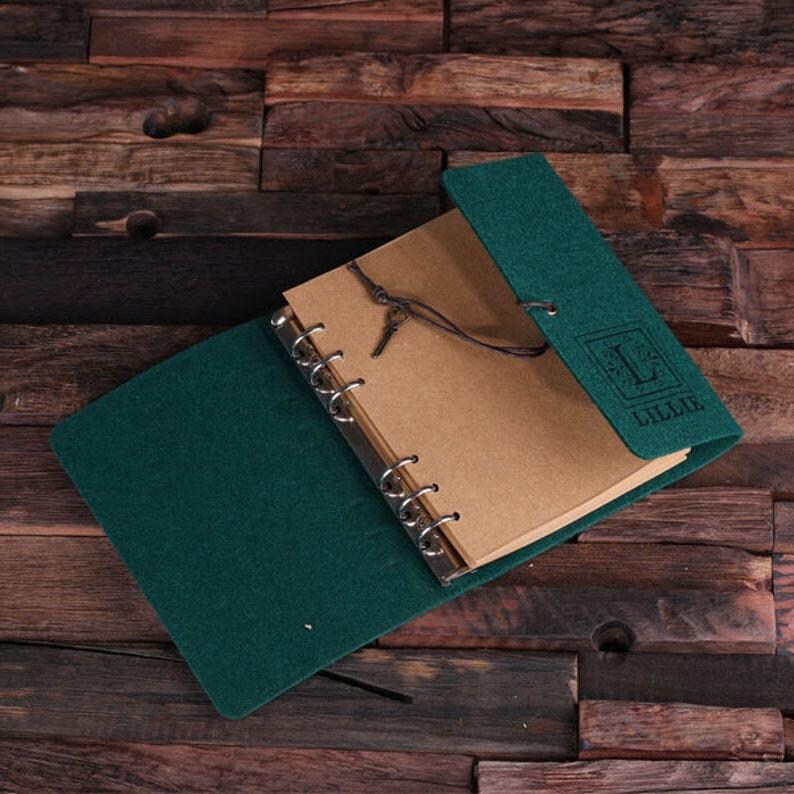 May include: A dark green felt-covered notebook with a brown paper insert and a metal ring binding. The notebook has a leather strap closure and a personalized inscription that reads "Lillie".
