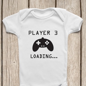 May include: White baby onesie with black text that reads "PLAYER 3 LOADING..." and a black video game controller graphic.