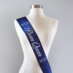 May include: A blue satin sash with silver glitter lettering that reads "WHS Prom Queen 2025".