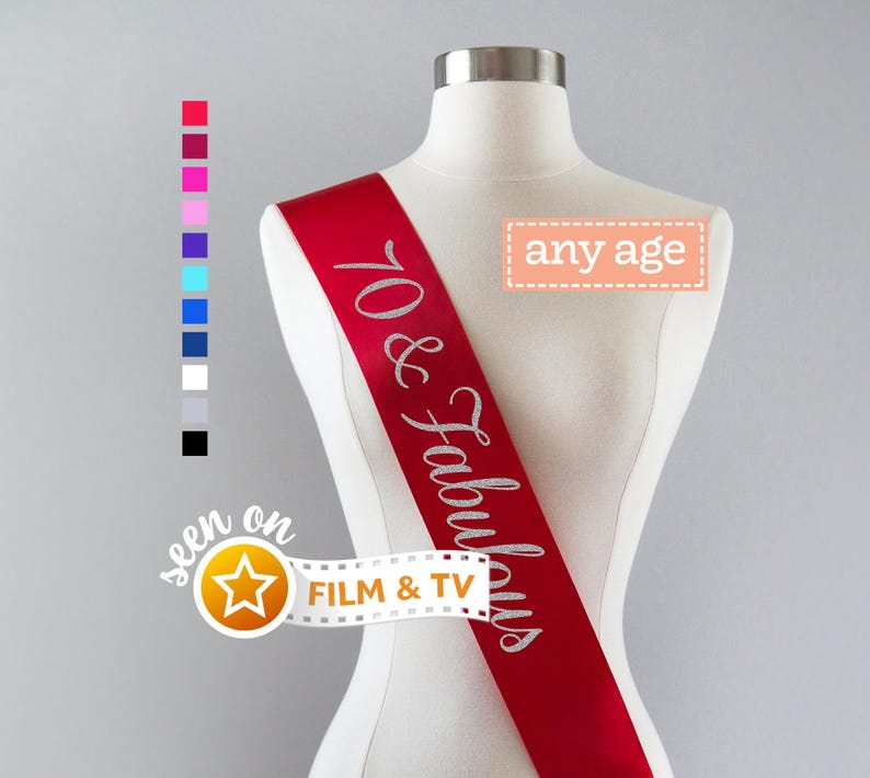 Pu&ograve; includere: Una fascia in raso rosso indossata su un busto di manichino, con la scritta in glitter argento 70 & Fabulous. Un riquadro rettangolare contiene il testo any age, e una grafica a pellicola include il testo seen on FILM & TV con una stella.