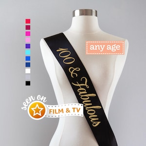 May include: A black satin sash worn across a mannequin torso, featuring gold glitter text that reads 100 & Fabulous. A vertical column of twelve small colored squares is displayed to the left, along with a rectangular box labeled any age.