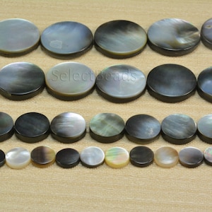 Puede incluir: Una colección de cuentas de nácar negro y blanco. Las cuentas son redondas y planas, y están dispuestas en filas. Las cuentas son de diferentes tamaños, siendo las más grandes de aproximadamente 2,5 cm de diámetro. Las cuentas son perfectas para hacer joyas u otras manualidades.