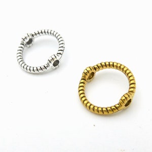 May include: Two metal rings, one silver and one gold, with a twisted rope design. The rings have two small holes on opposite sides.