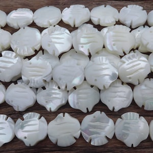 Może przedstawiać: Szereg białych pereł z masy perłowej, każda perła jest rzeźbiona w kształcie ryby z detalicznym wzorem.