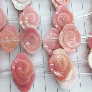 May include: A strand of pink and white shell rose beads strung on clear elastic cord. The beads are all in the shape of a rose with a swirl pattern.