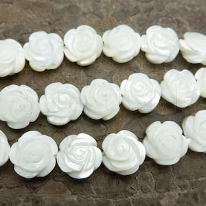 May include: A strand of white mother of pearl rose beads. The beads are carved in the shape of roses and have a pearlescent finish.