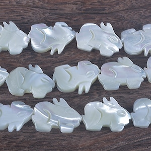 May include: A strand of white mother-of-pearl beads, each bead is carved in the shape of a rabbit. The beads are arranged in three rows on a wooden surface.