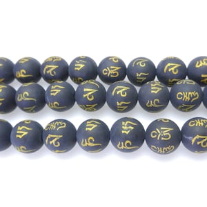 May include: Strand of dark blue matte beads with gold-colored script. The round beads are evenly sized and strung together, creating a symmetrical pattern. The gold script adds a decorative element to the beads.