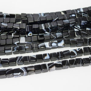 May include: Black and white agate square beads. The beads have a polished finish and are strung together on a string.