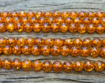 May include: A strand of amber beads, with a warm, honey-like color, arranged in three rows on a rustic wooden surface.