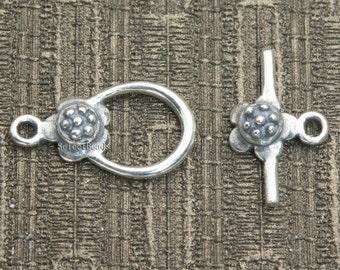 May include: Silver toggle clasp with a flower design. The clasp has a round loop on one side and a bar with a loop on the other side.