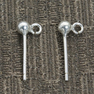 Pode incluir: Um par de postes de brincos de prata com um pequeno laço na parte superior. Os postes medem aproximadamente 2,5 cm de comprimento.