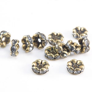 May include: A group of antique gold-toned metal beads with clear rhinestone accents. The beads are round and have a flower-like design.