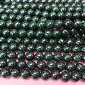 May include: A close-up of a strand of dark green round beads with a glittery finish.
