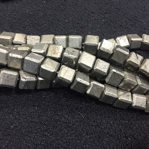 Könnte beinhalten: Eine Strähne aus Pyritperlen, jede Perle ist ein Würfel mit einer metallisch silbernen Farbe und einer leicht rauen Textur.