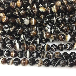 May include: A strand of black and white agate beads. The beads are round and have a smooth, polished finish. The agate is a natural stone with a unique pattern of black and white stripes.