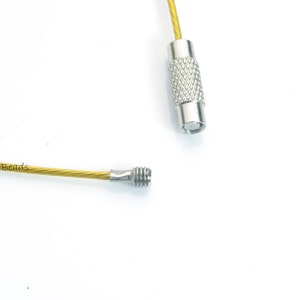 May include: A gold-colored metal cable with silver-colored metal ends. The cable is flexible and has a slight twist. The ends are threaded and can be used to attach to other objects.