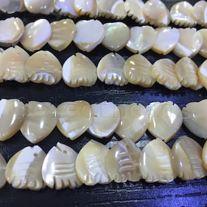 Può includere: Una collana di perle di conchiglia bianca e beige a forma di cuore con un design intagliato. Le perle sono infilate su un cordoncino bianco.