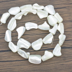 May include: A strand of white, iridescent, shell beads in a circular shape. The beads are smooth and have a natural, organic look.