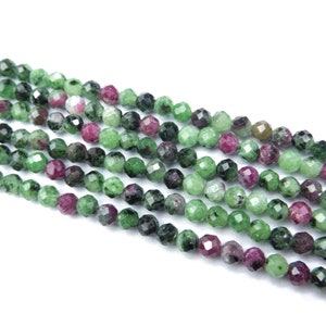 May include: A strand of green and pink faceted gemstone beads. The beads are round and have a polished finish.
