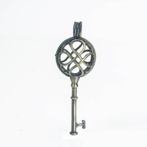 May include: A bronze key-shaped pendant with a circular, openwork design featuring a four-leaf clover motif.