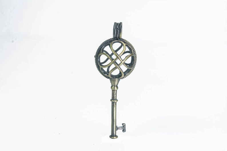 May include: A bronze key-shaped pendant with a circular, openwork design featuring a four-leaf clover motif.
