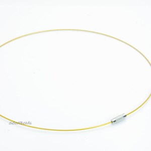 May include: A gold-colored, thin, flexible wire necklace with a silver clasp. The necklace is lying flat on a white surface.