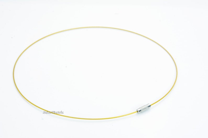 May include: A gold-colored, thin, flexible wire necklace with a silver clasp. The necklace is lying flat on a white surface.