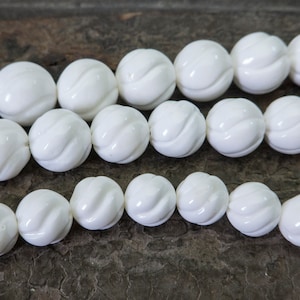 Op de afbeelding: Een streng witte keramische kralen met een gegraveerd ontwerp. De kralen zijn rond en hebben een gladde, gepolijste afwerking.