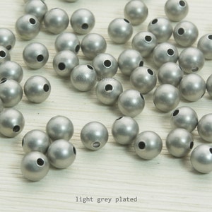 May include: A collection of light grey plated round beads with a matte finish. Each bead has a hole for stringing. The text "light grey plated" is visible at the bottom of the image. These beads are suitable for jewelry making.