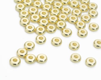 May include: A large quantity of gold-colored metal beads, scattered on a white surface. The beads are round with a hole in the center.