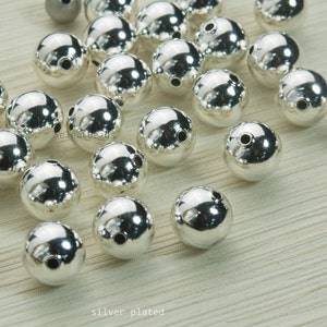May include: A collection of shiny, silver-plated beads. Each bead is spherical with a smooth, reflective surface and two small holes. The beads are scattered, with the text "silver plated" at the bottom.