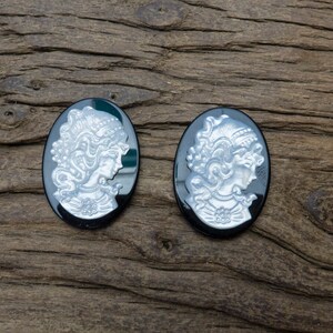 May include: Two black cameo pendants with silver-toned raised images of women's profiles. The pendants are oval shaped and have a smooth, glossy finish.