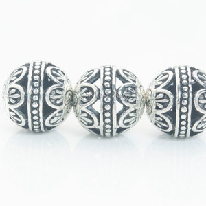 May include: Three silver beads with intricate, ornate designs. The beads are round and have a raised, textured pattern.