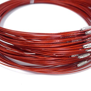 May include: A close-up of a bundle of red, thin, metal cable necklaces with silver clasps. The necklaces are coiled together and are ready to be used for jewelry making.