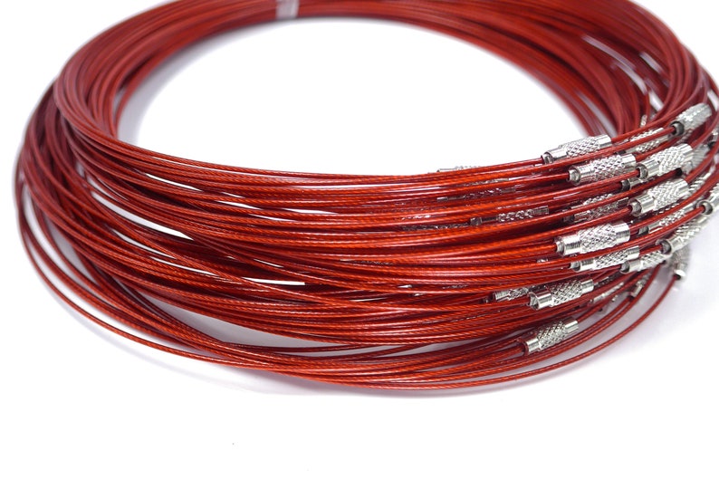 May include: A close-up of a bundle of red, thin, metal cable necklaces with silver clasps. The necklaces are coiled together and are ready to be used for jewelry making.