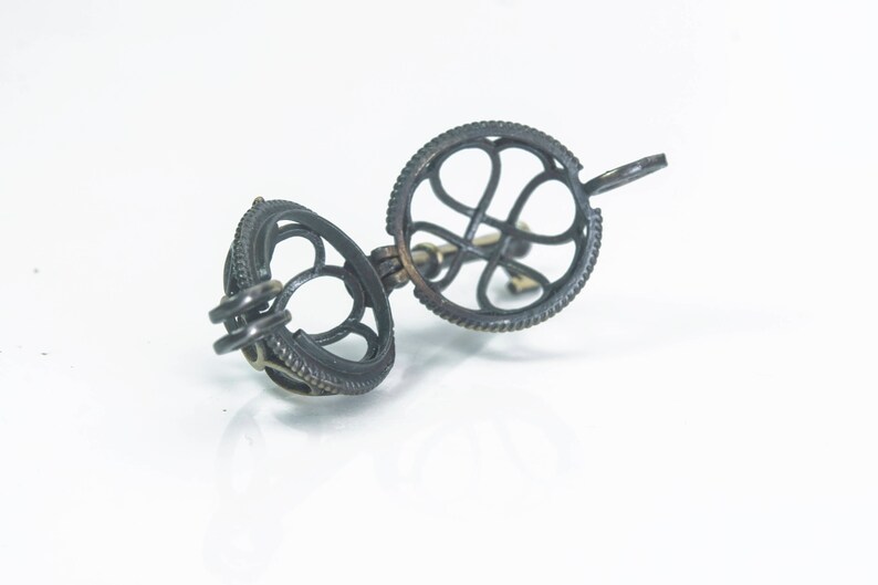 May include: A silver charm with a cage design. The cage is open on one side and has a small loop on the other side for attaching to a bracelet or necklace.