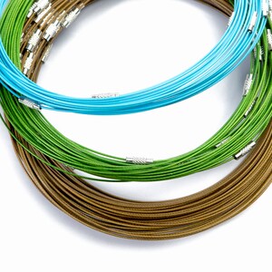 May include: Three spools of wire, one brown, one green, and one aqua, are stacked on top of each other. The spools are made of thin wire and have a shiny finish.