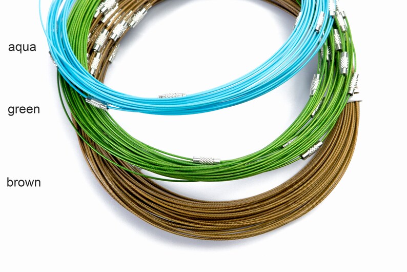 May include: Three spools of wire, one brown, one green, and one aqua, are stacked on top of each other. The spools are made of thin wire and have a shiny finish.