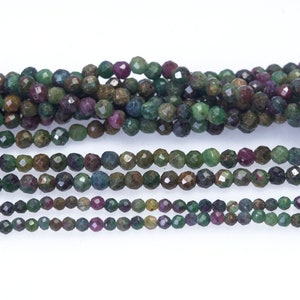 May include: A strand of faceted gemstone beads in shades of green, brown, and red. The beads are small and round, and they are strung together on a clear thread.