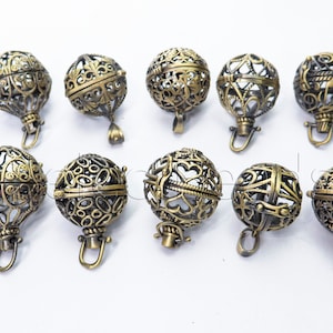 Op de afbeelding: Tien antieke goudkleurige metalen kooi-hangers met ingewikkelde ontwerpen. Elke hanger heeft een scharnierende opening en een lus om op te hangen.